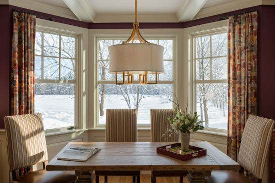 A table situated strategimcally before large windows provides a serene place to work on a snowy afternoon. source:  Karosis Photograhy