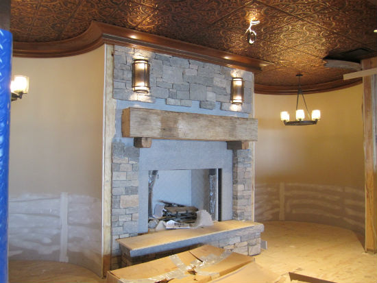 An inglenook in the dining room.  The mantle is made from a reclaimed barn beam from Maine.  The will eventual;ly be a circular banqueet flanking the fireplace. The ceiling is copper-colored tin.  Source:  TMS Architects